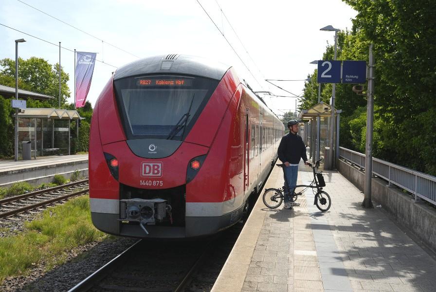 Das Bild zeigt einen Mann mit einem Brompton Klapp e-Bike C-Line an einem Zug