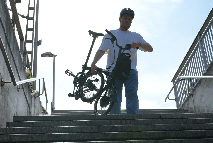 Das Bild zeigt einen Mann, der ein Brompton Klapp e-Bike C-Line eine Trepper herunter trägt
