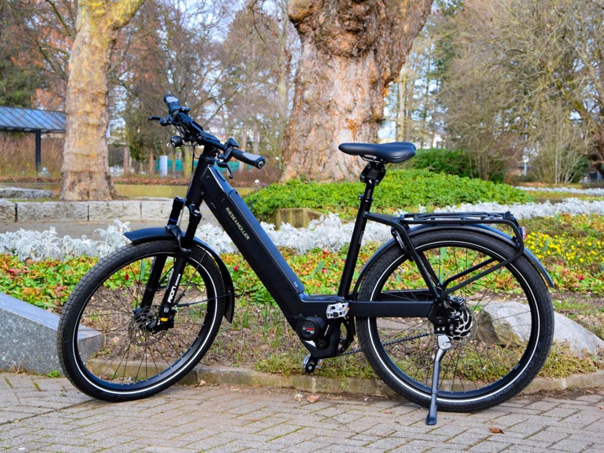 Das Bild zeigt ein Riese & Müller Nevo3 GT e-Bike, das in einem parkähnlichen Umfeld abgestellt ist. Das Fahrrad ze