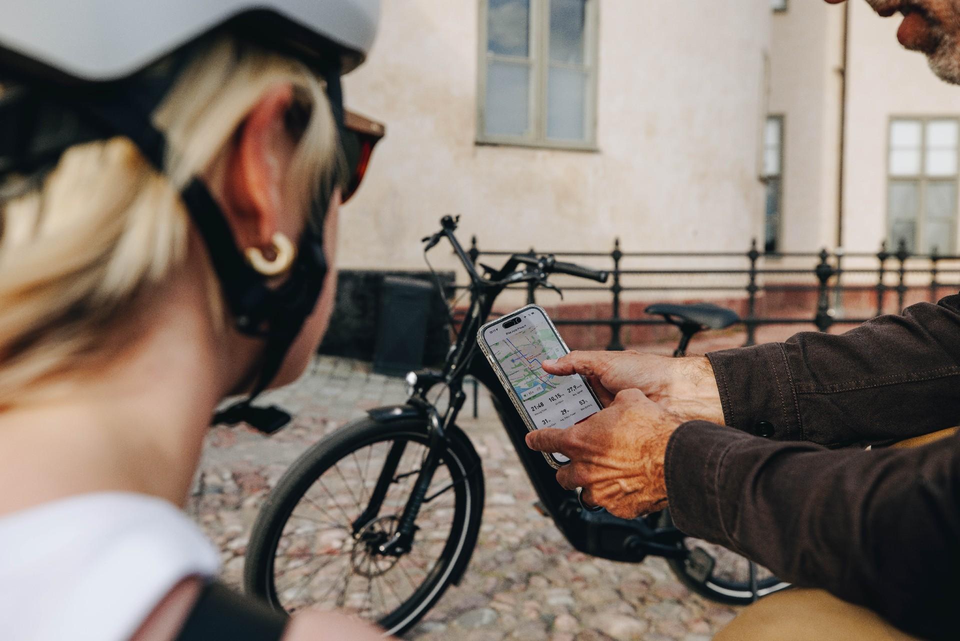 Zwei Personen schauen ein Handy, im Vordergrund eine Frau mit Helm, im Hintergrund ein Specialized e-Bike