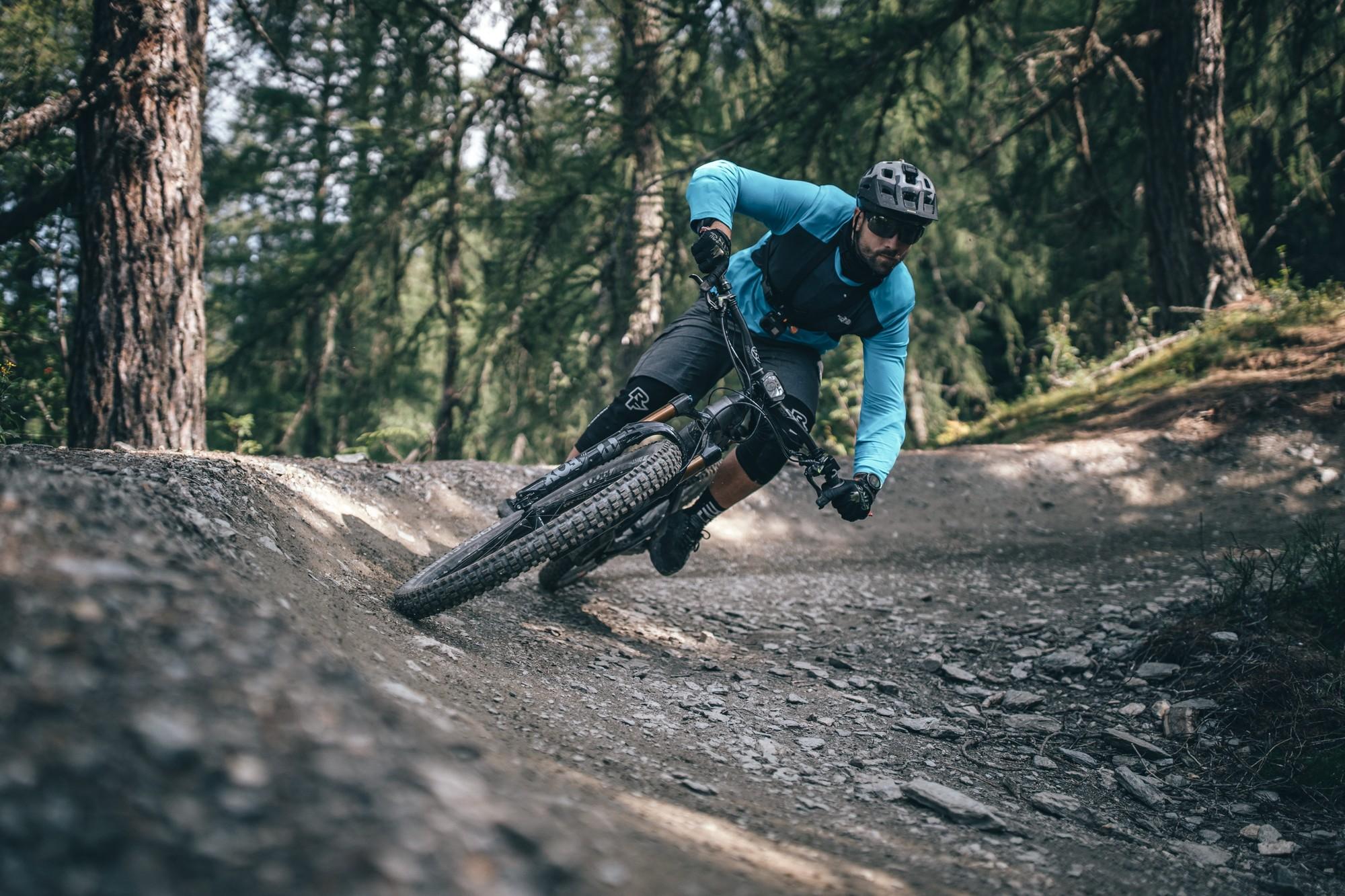 Das Bild zeigt einen sportlichen Mountainbiker, der auf einem schmalen, kurvenreichen Waldweg fährt.