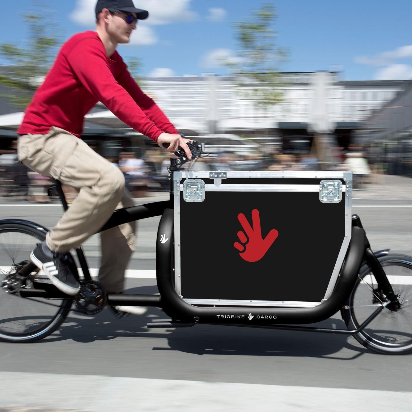 Ein Mann fährt auf dem Lastenrad Triobike Cargo schnell die Straße entlang