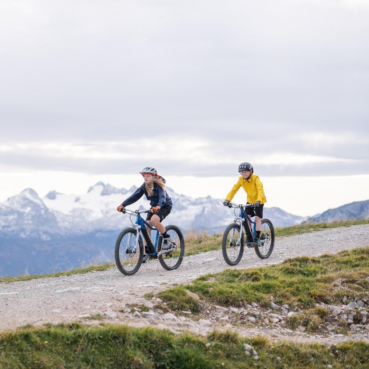 Zwei Kinder auf Woom e-Bikes in der Natur, Berge im Hintergrund