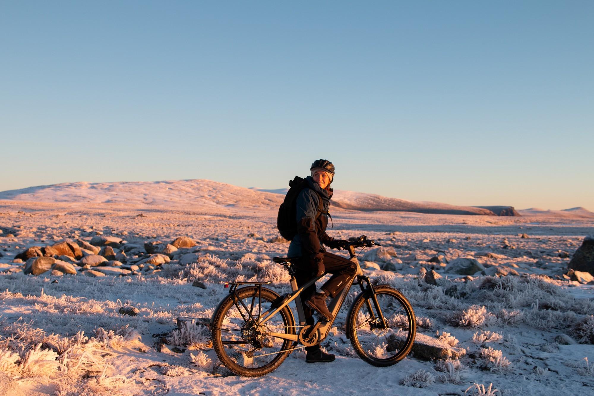 Eine Frau steht mit ihrem e-Mountainbike von Kalkhoff in winterlicher Landschaft und es liegt Schnee.