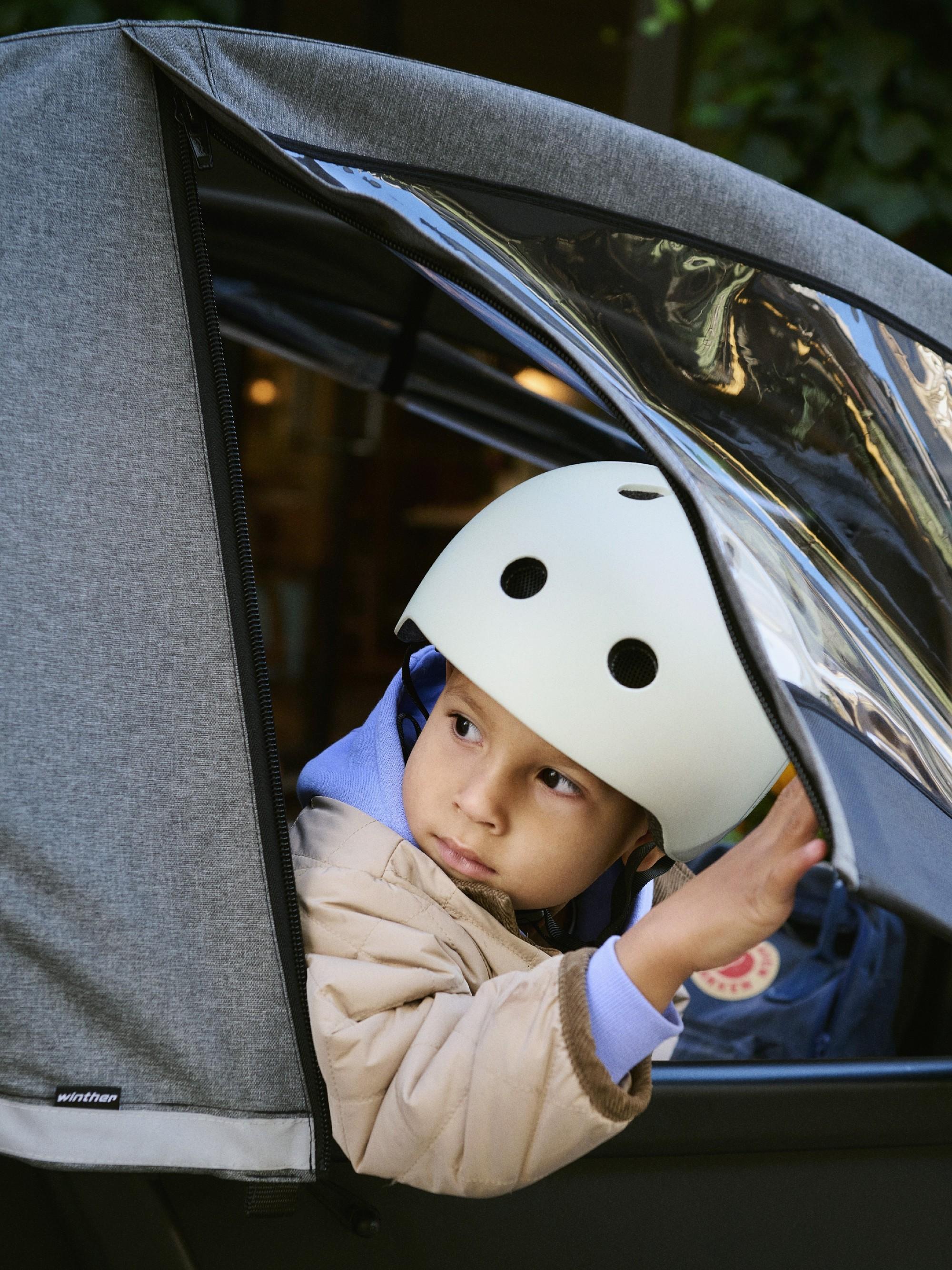 Ein Kind mit Helm schaut aus der Transportbox des Lastenrads von Winther