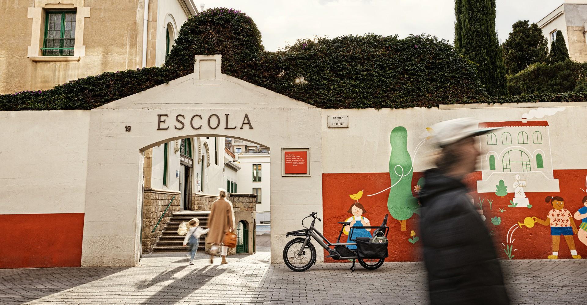 Das Specialized Porto Turbo steht vor einer Schule, durch den Eingang gehen Hand in Hand Frau und Kind