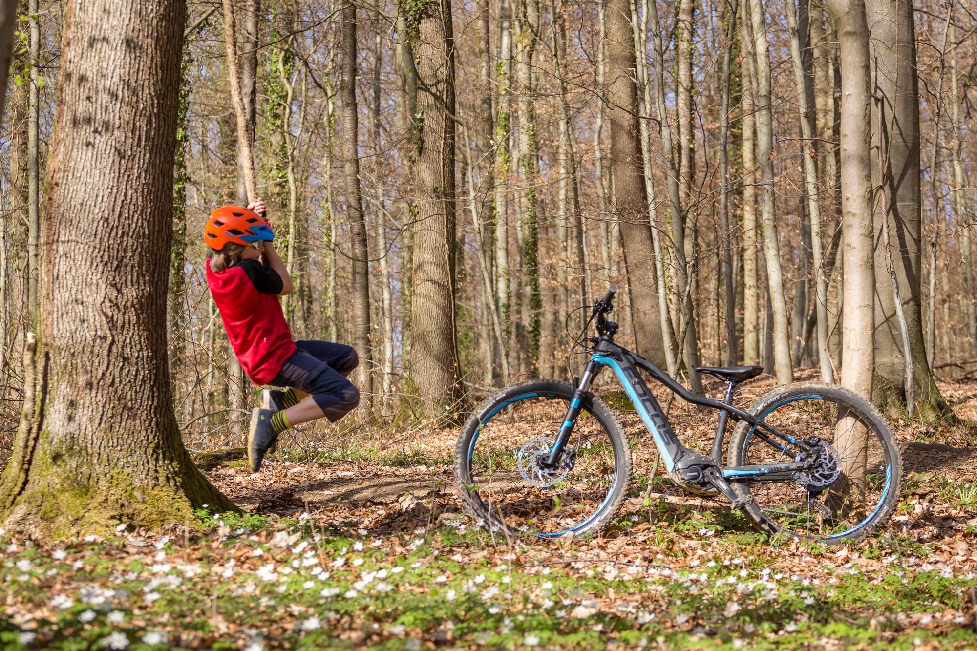 Das Bild zeigt ein Focus Bold² XS E-Bike, das in einem Waldgebiet abgestellt ist.