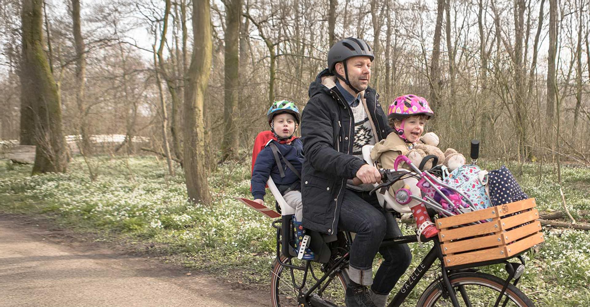 Ein Vater fährt mit seinen Kindern auf einem Gazelle Family Bike durch einen Wald
