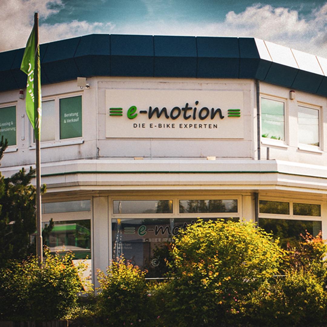 Die Außenfassade der e-motion e-Bike Welt mit einem Fahnenmast und grünen Akzenten