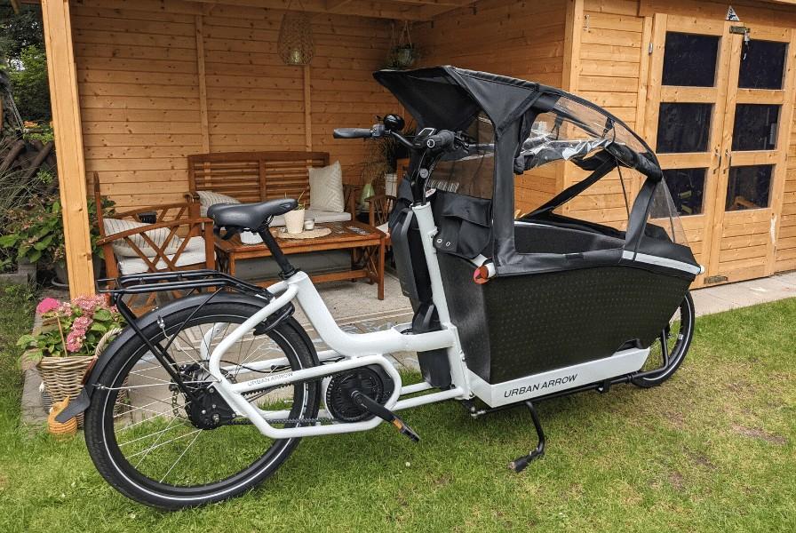 Das Bild zeigt ein Urban Arrow Family mit Regenverdeck im Garten
