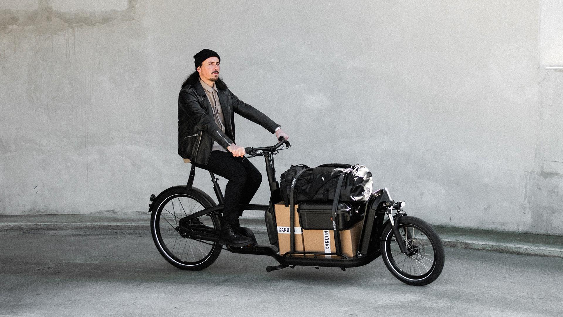 Ein Mann fährt mit dem Lasten e-Bike Carqon Flatbed und Ladung die Straße entlang