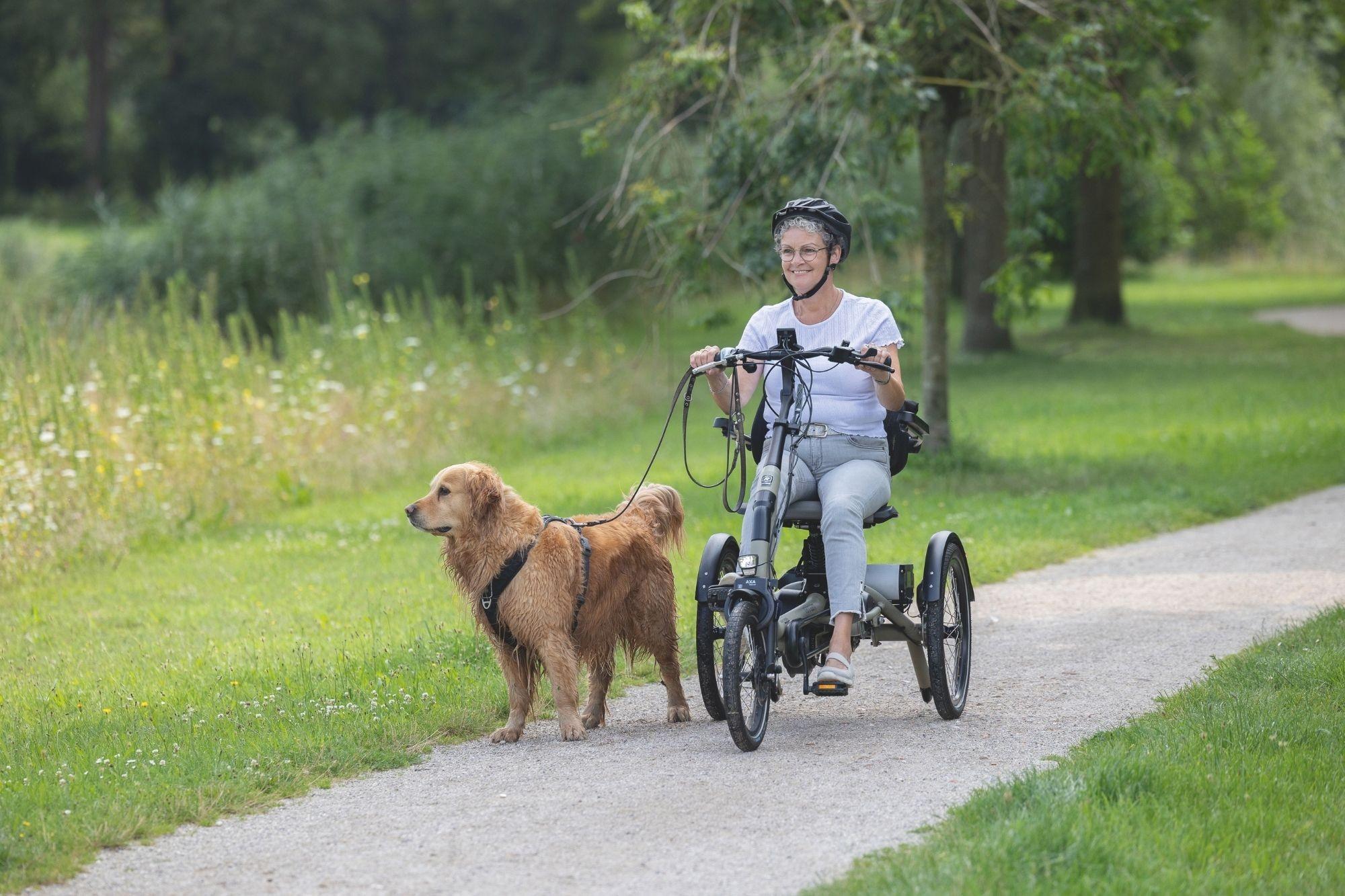 Eine Frau sitzt auf dem vanRaam Easy Rider Compact Dreirad und hat einen Hund an der Leine