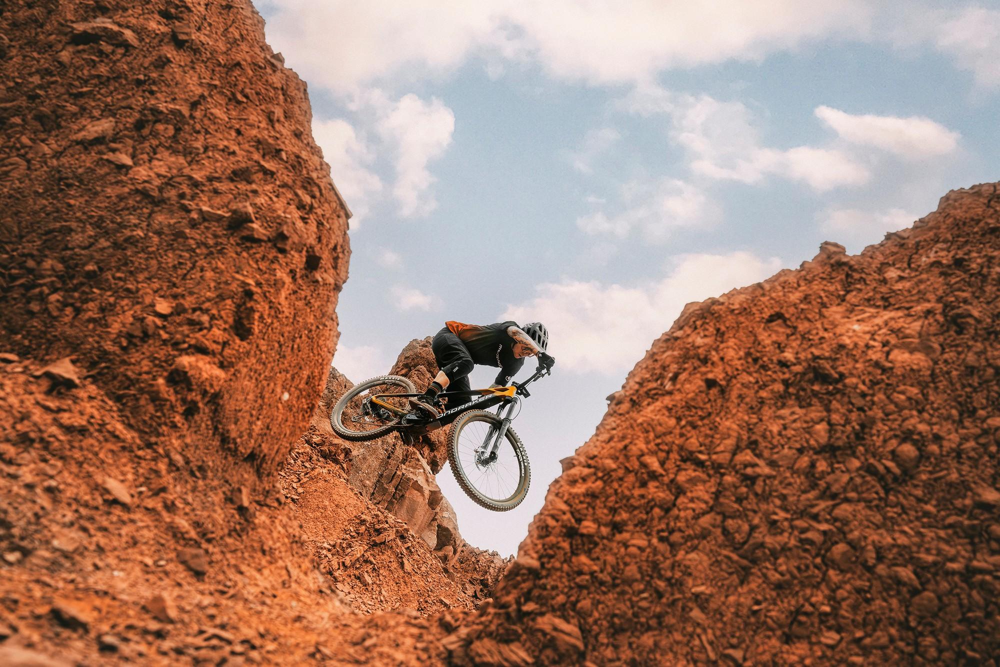 Das Bild zeigt ein Mountainbike, das Modell Mondraker Dune, während es durch eine felsige Passage fährt. Der Fahrer