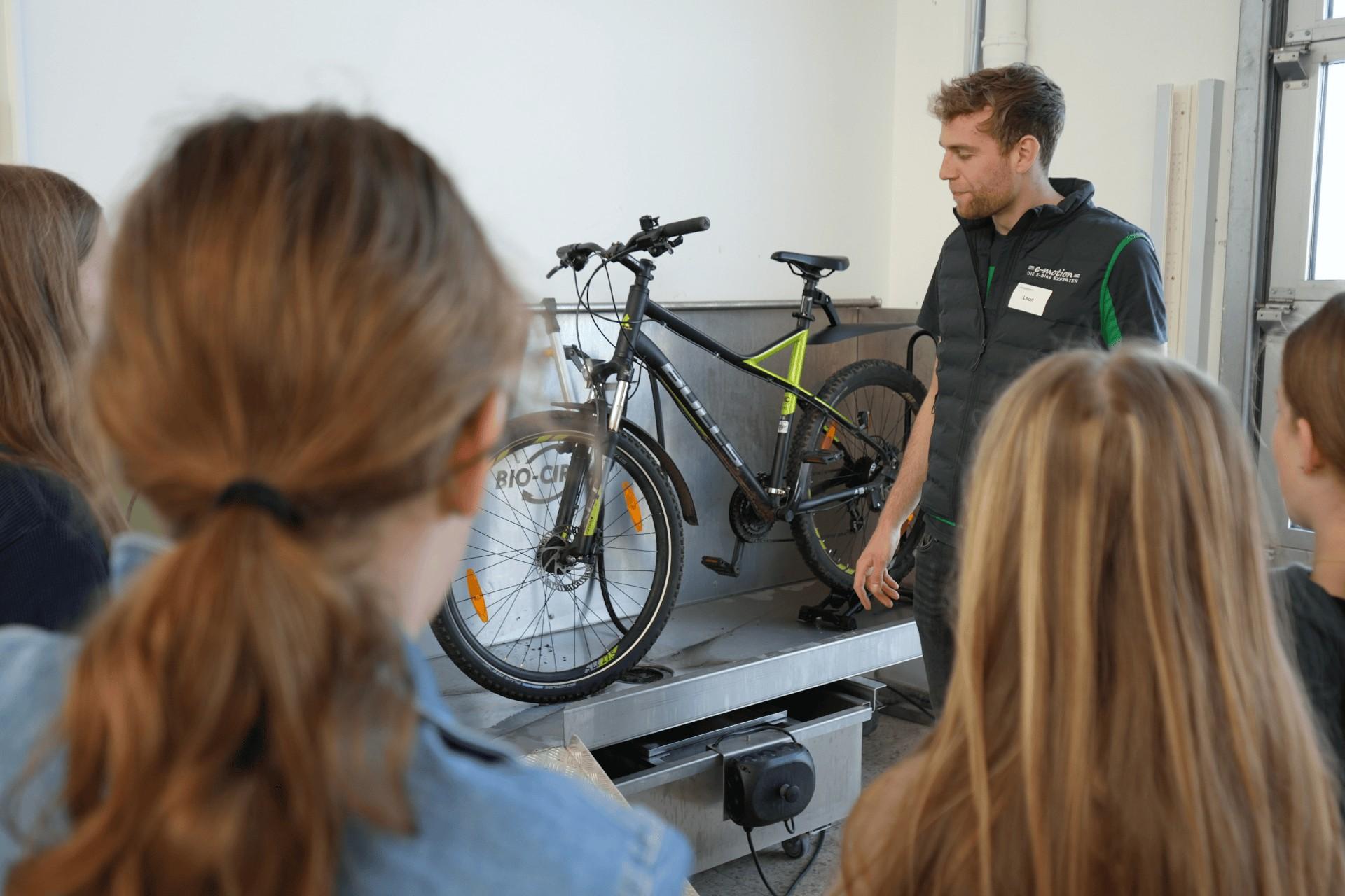 Teilnehmerinnen und Leon stehen vor e-Bike, der Werkstattmitarbeiter gibt Infos zum e-Bike