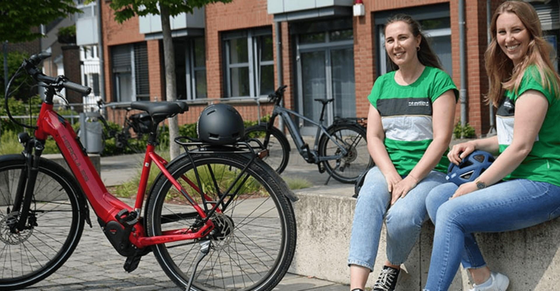 Zwei Frau sitzen mit einem Hercules e-Bike auf einer Steinmauer