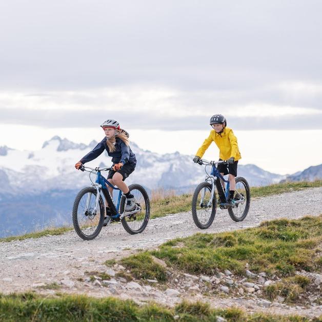 Zwei Kinder auf Woom e-Bikes in der Natur, Berge im Hintergrund
