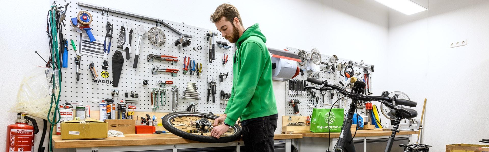 E-Motion Mitarbeiter vor Werkstattwand arbeitet an einem Hinterrad.