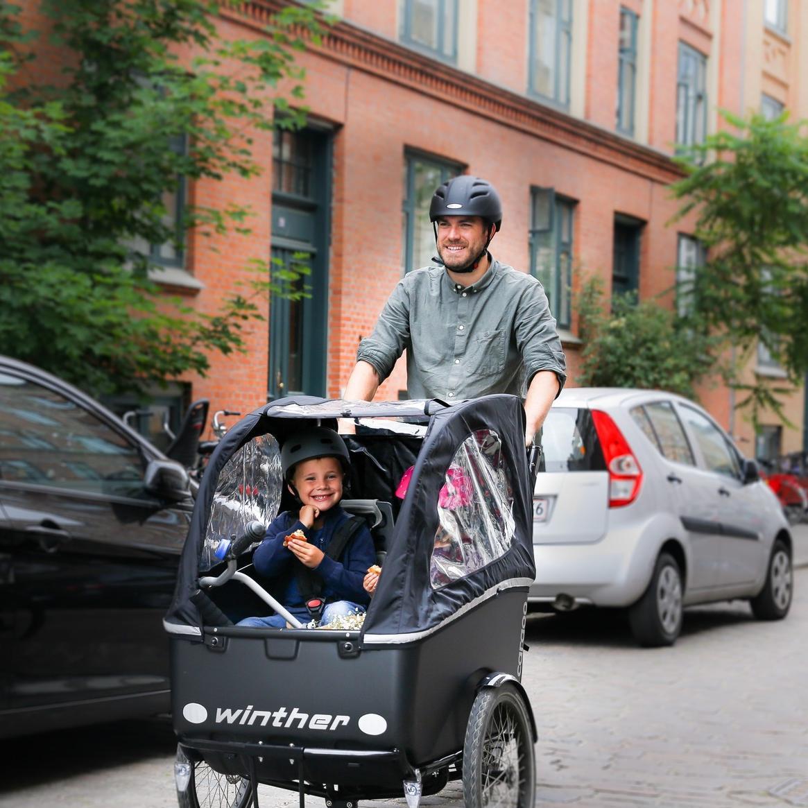 Ein Mann fährt mit seinem Winther Lastenrad und seinen Kindern in der Transportbox