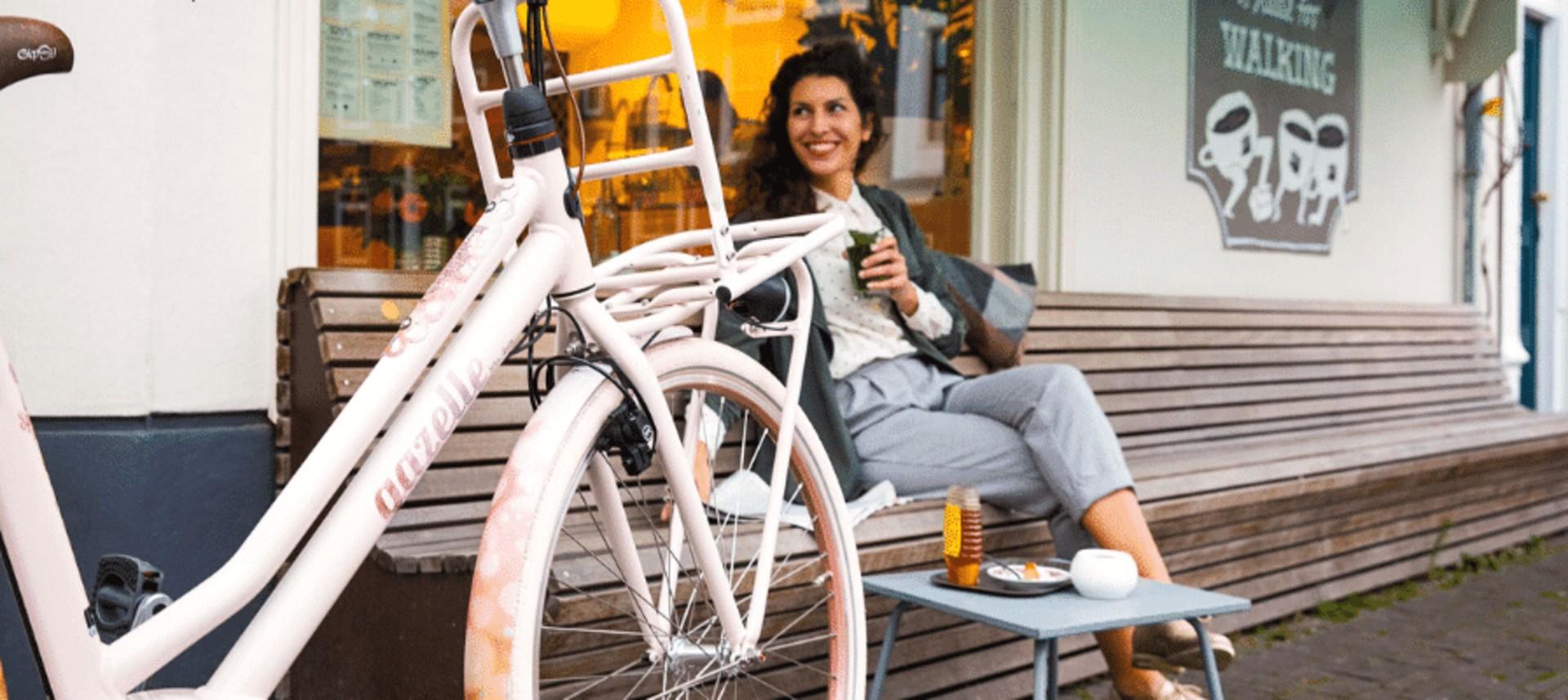 Auf dem Bild ist eine Frau zu sehen, die entspannt neben einem Gazelle Miss Grace e-Bike sitzt.