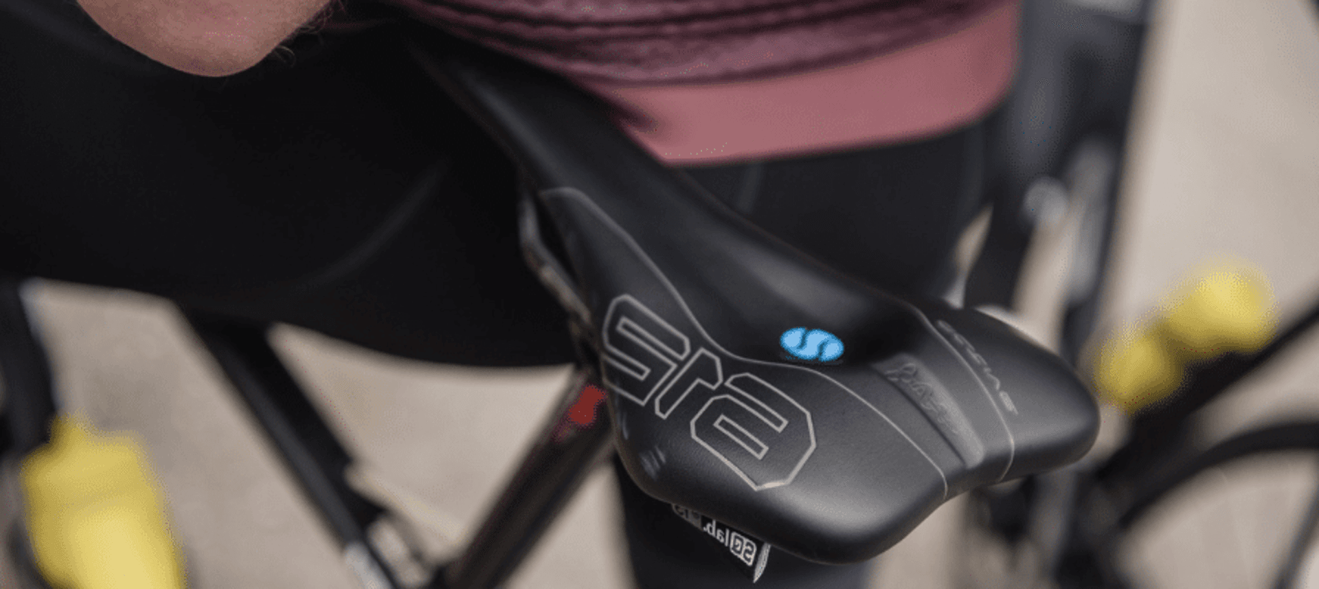 Nahaufnahme eines schwarzen SQLab-Sattels 612, im Hintergrund unscharf Radfahrer und gelbe Trinkflaschen.