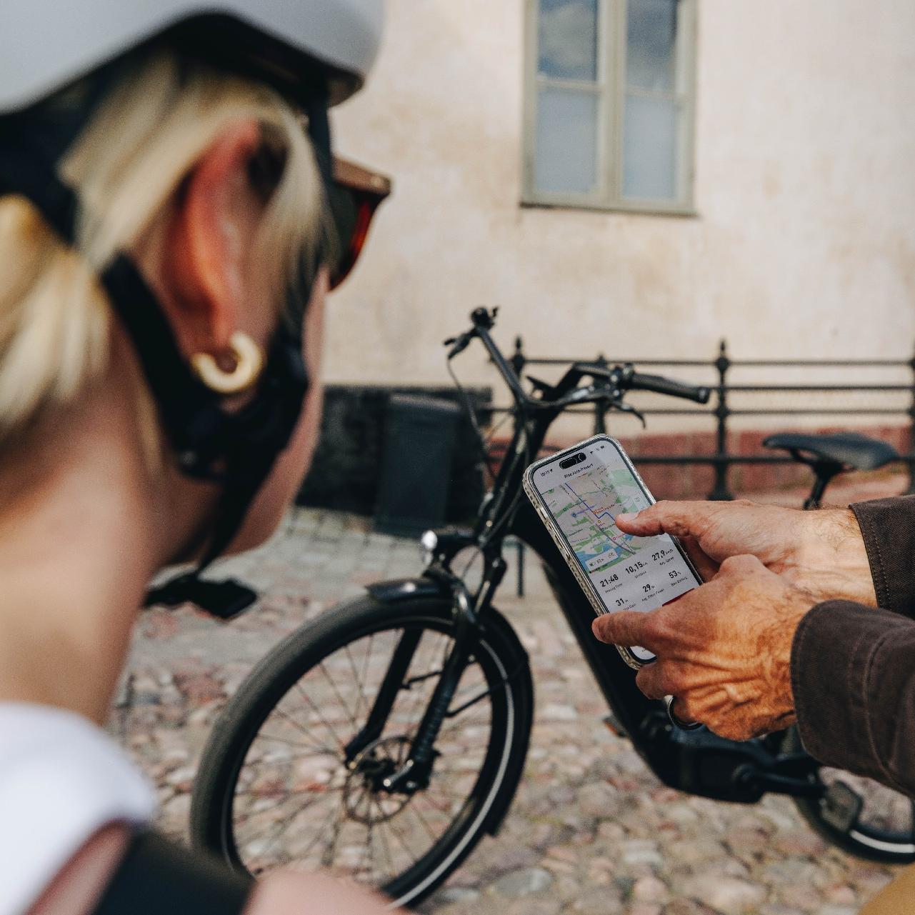 Zwei Personen schauen ein Handy, im Vordergrund eine Frau mit Helm, im Hintergrund ein Specialized e-Bike