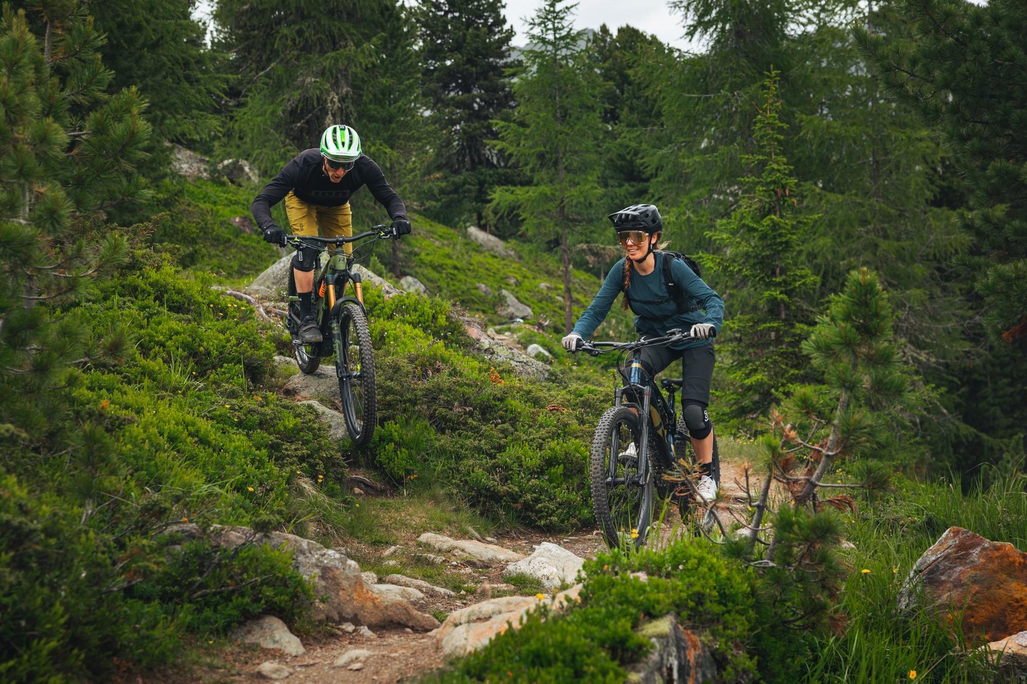 Ein Mountainbiker-Paar fährt auf dem R Raymon Fullray e-Nine Trailbike einen Berg herunter.
