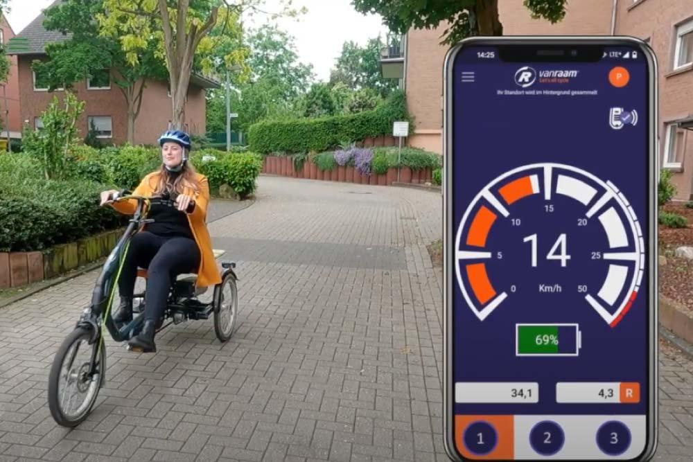 Eine Frau sitzt auf einem vanRaam Dreirad, daneben zu sehen die vanRaam App mit Infos zur Geschwindigkeit und Akku