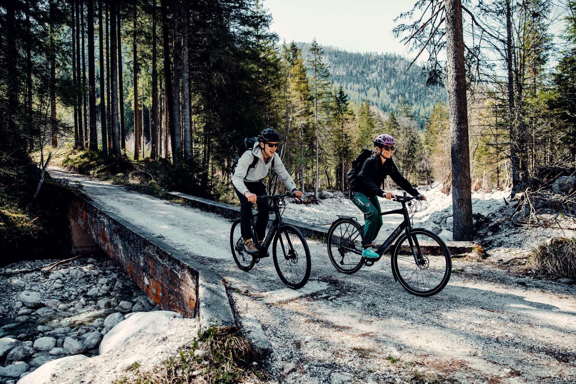 Zwei Personen fahren auf E-Bikes durch einen Wald. Ideal für Naturbegeisterte, die Abenteuer und frische Luft suche