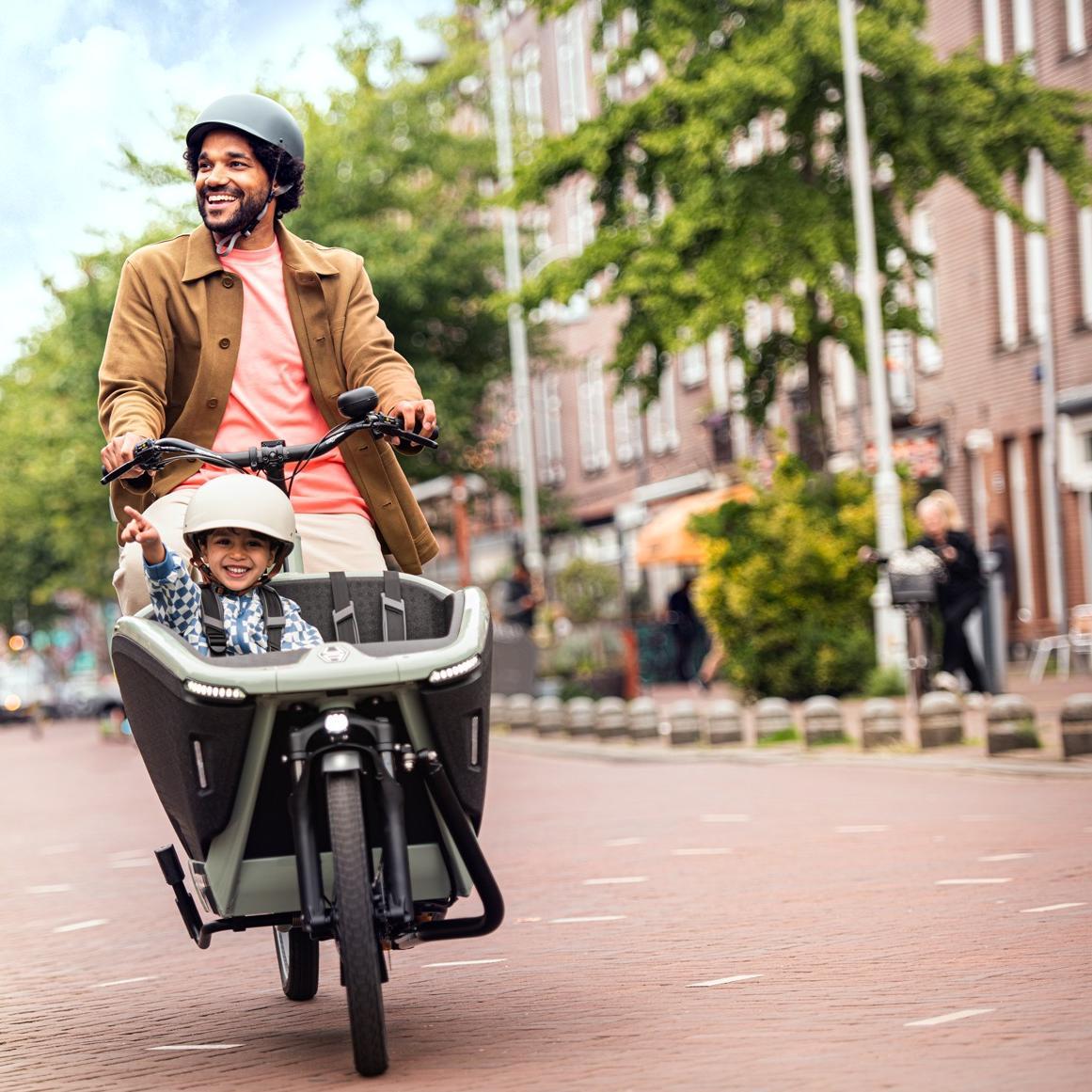 Ein Mann fährt sein Kind im Lastenrad von Urban Arrow durch die Straßen