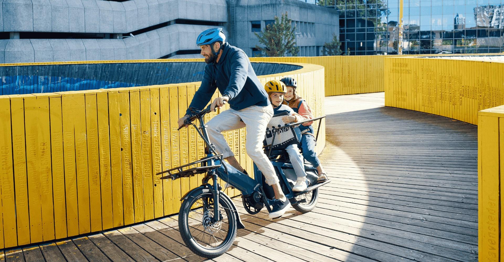 Ein Mann fährt auf dem Riese und Müller Multitinker, hinten auf dem Gepäckträger sitzen zwei Kinder