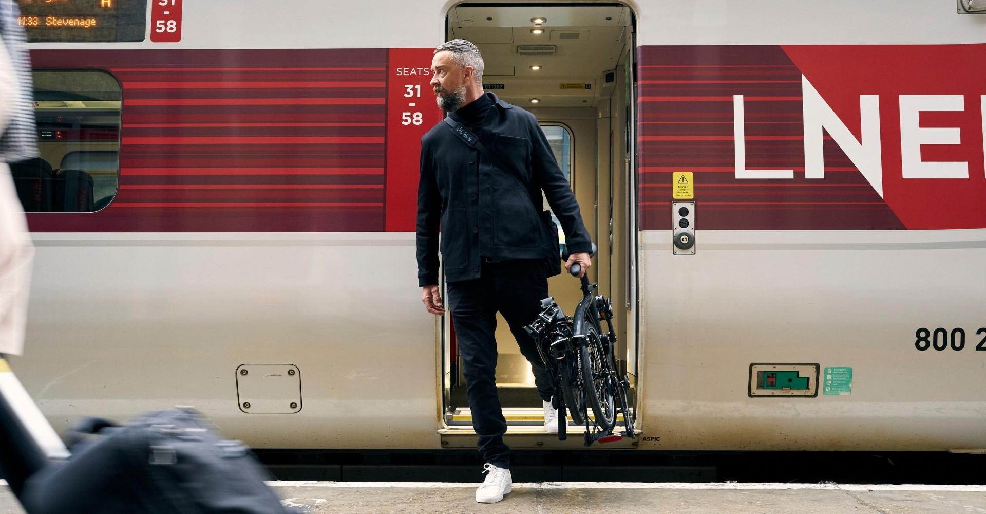 Mann steigt aus Zug mit dem Kompakt e-Bike P Line Brompton