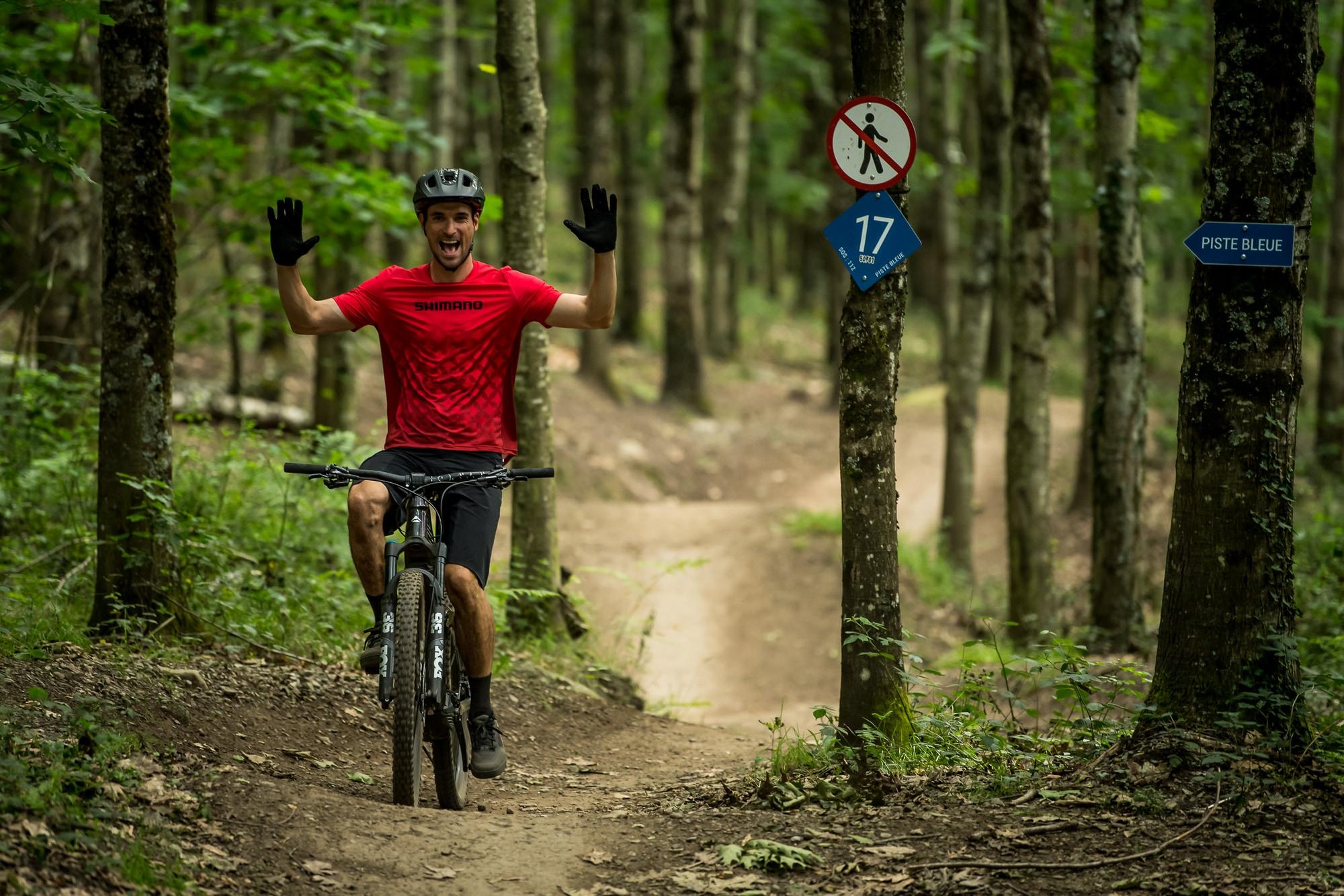 Ein Mann steht mit seinem e-Mountainbike neben einem Schild am Baum