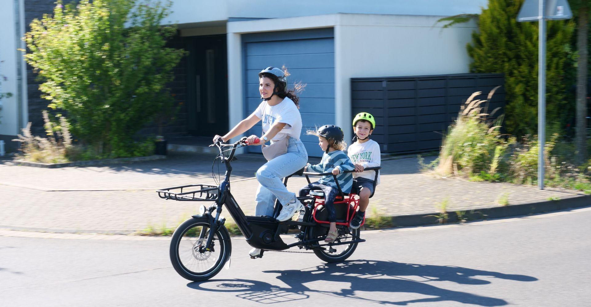 Eine Frau sitzt auf dem Cannondale Cargowagen Neo 1 im Test hinten auf dem Gepäckträger zwei Kinder
