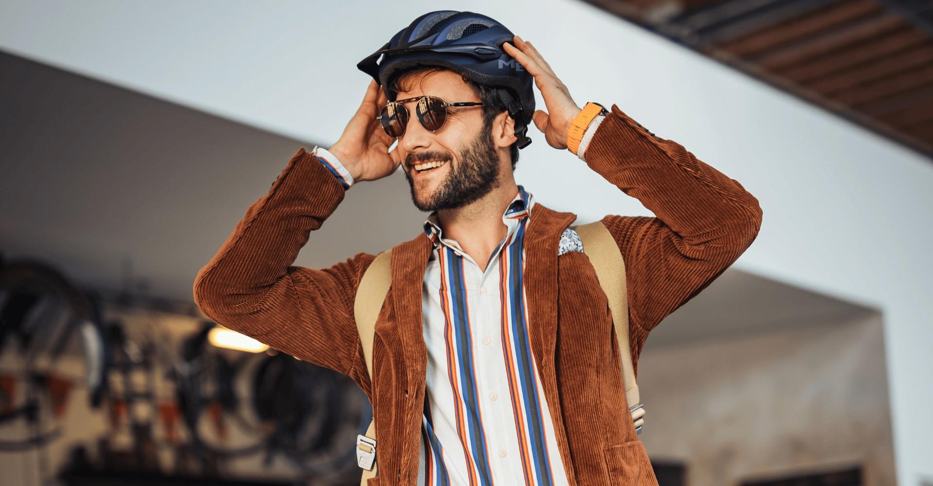 Ein Mann zieht einen Helm auf, er trägt dazu eine Sonnenbrille und Rucksack