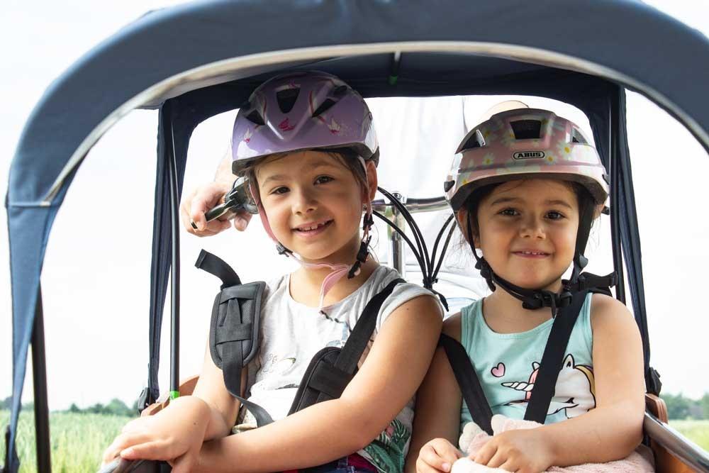 Zwei Mädchen sitzen mit Helmen in der Transportbox des Babboe Lastenrads