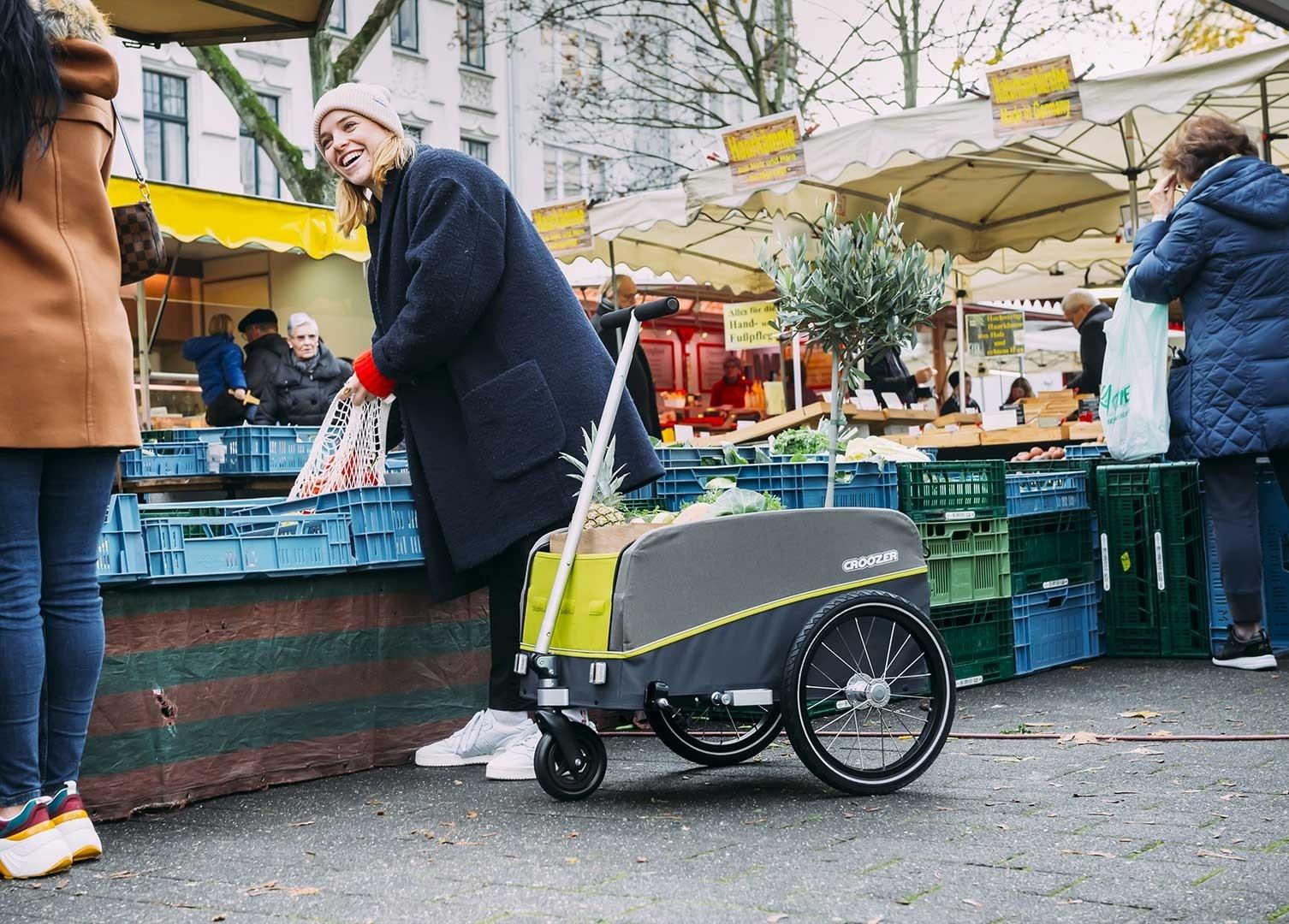 Das Bild zeigt eine Frau bei einem Einkauf auf dem Markt mit einem Croozer Anhänger