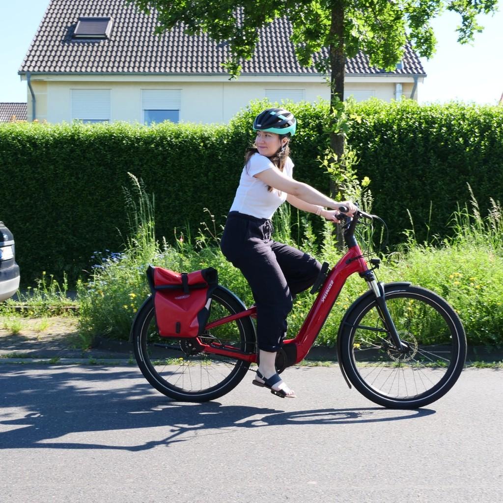 Fahrerin auf einem eleganten roten E-Bike, entspannt durch die Straße gleitend, ideal für urbane Mobilität und umwe