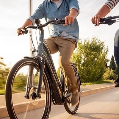 Zwei Personen fahren auf modernen E-Bikes auf einer Straße bei Sonnenuntergang