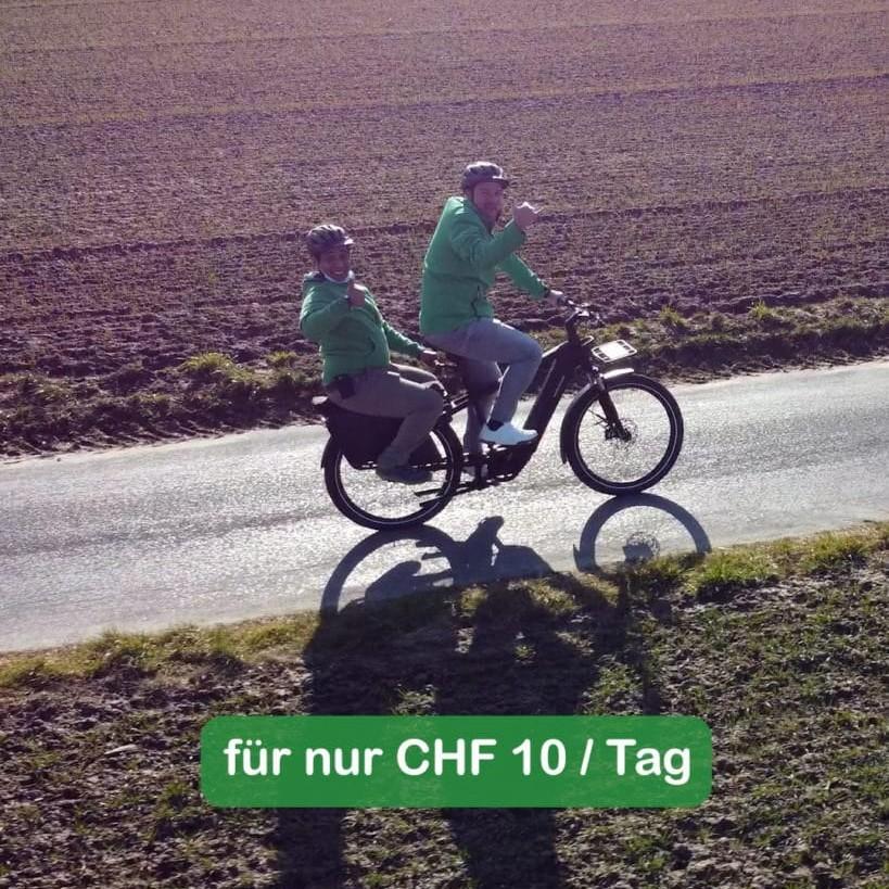 Zwei Personen auf E-Bike auf ländlicher Straße mit Werbetext