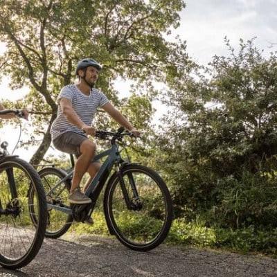 Zwei Personen fahren E-Bikes auf einem ländlichen Weg bei sonnigem Wetter