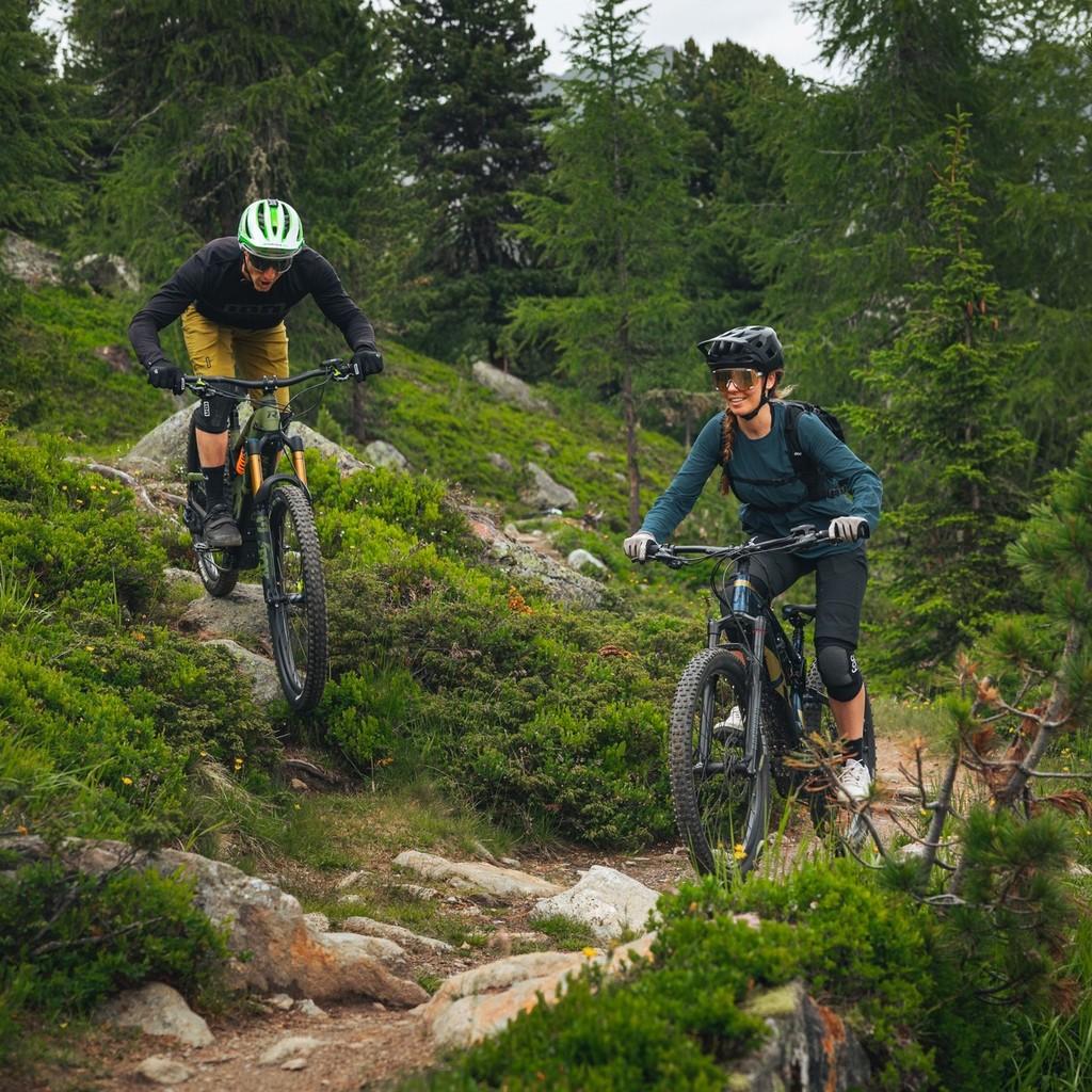 Ein Mountainbiker-Paar fährt auf dem R Raymon Fullray e-Nine Trailbike einen Berg herunter.
