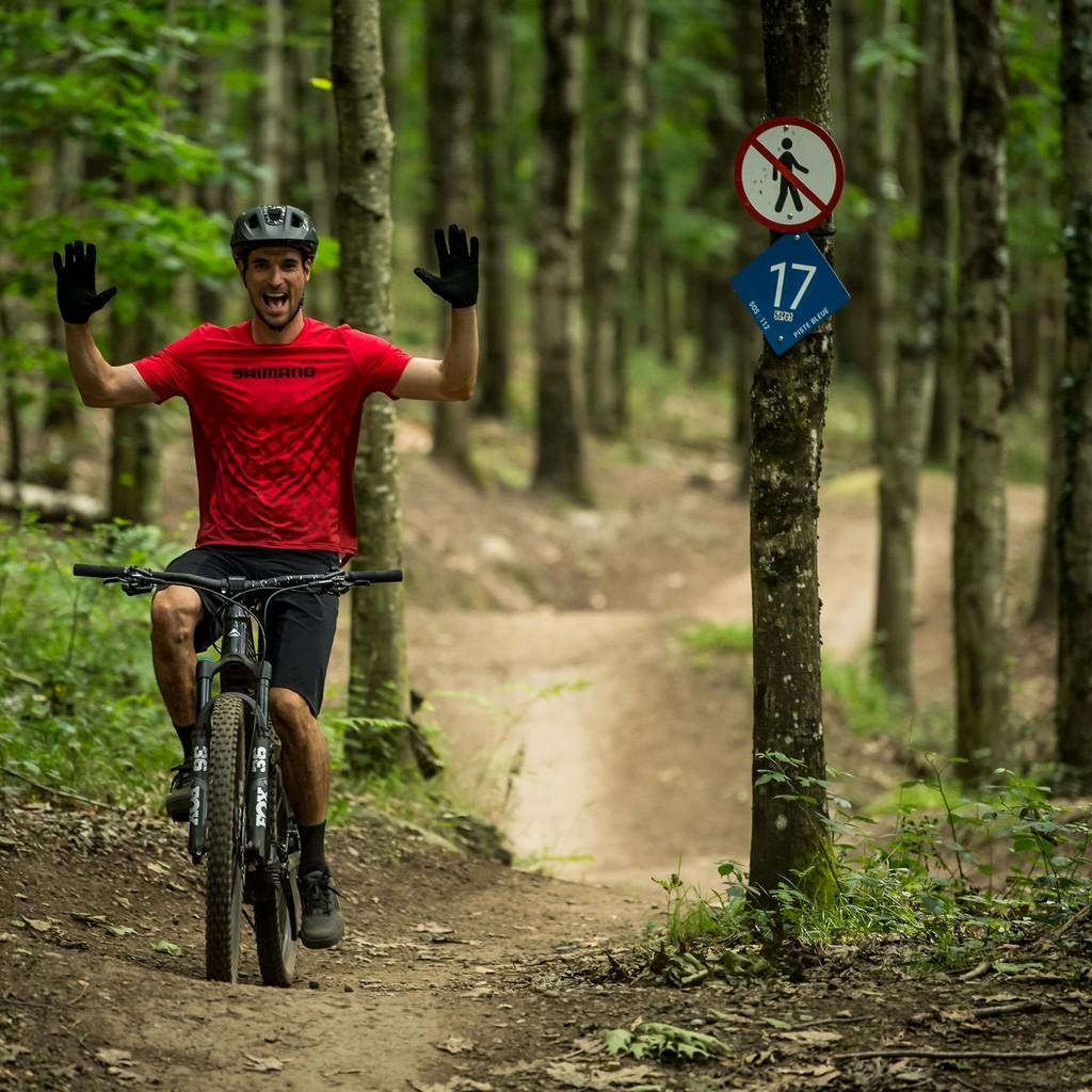 Ein Mann steht mit seinem e-Mountainbike neben einem Schild am Baum