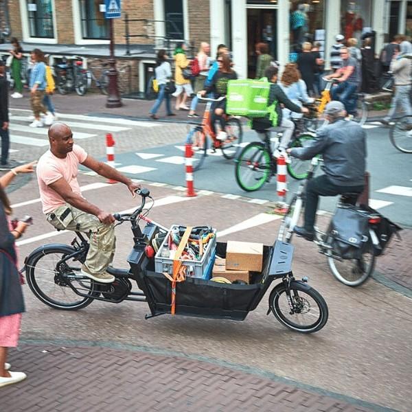 Mann fährt Lastenrad mit Paketen in belebter Stadtstraße