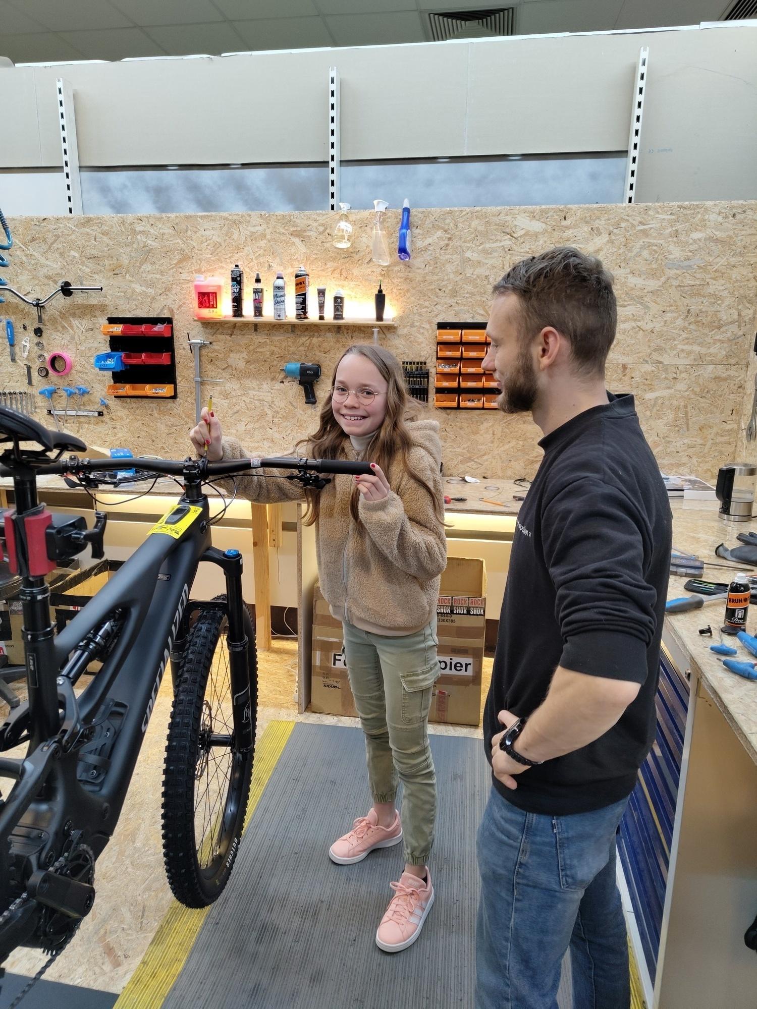 Das Bild zeigt eine Interaktion zwischen einem jungen Mädchen und einem männlichen Betreuer in einer Werkstatt für