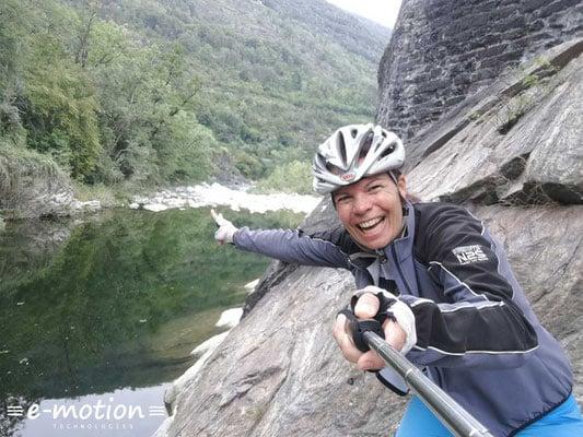 Frau mit Selfie-Stick zeigt auf Fluss in bergiger Landschaft