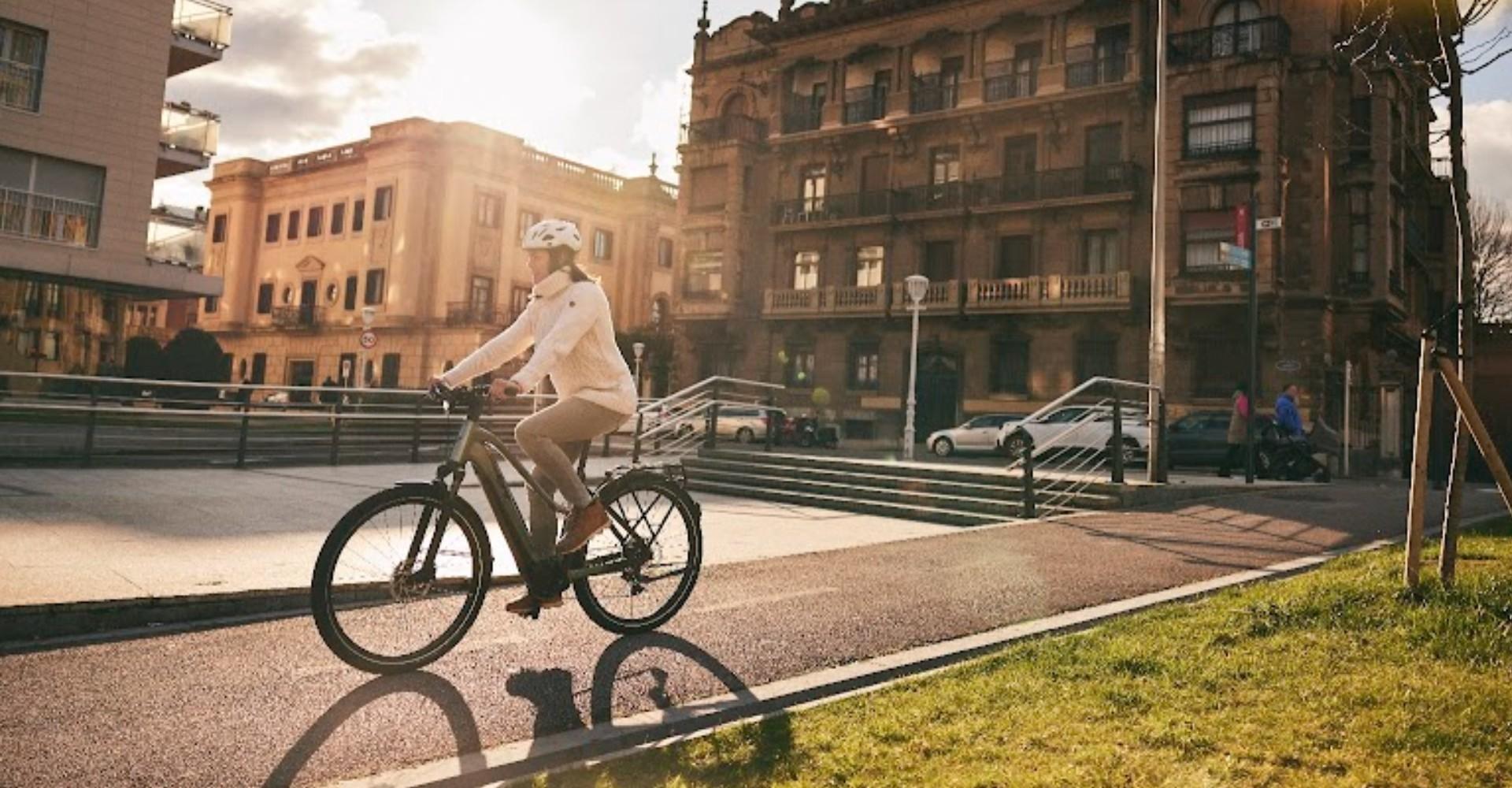 Das Bild zeigt ein Liv Amiti E+ Trekking e-Bike, das von einer Person in einer städtischen Umgebung gefahren wird.