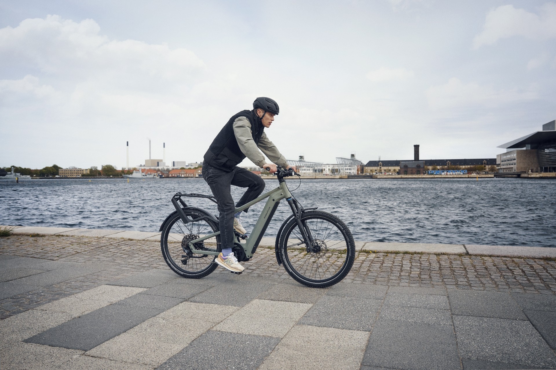 Riese & Müller Delite4 in Grau wird von einer Person mit Helm entlang eines Gewässers gefahren.