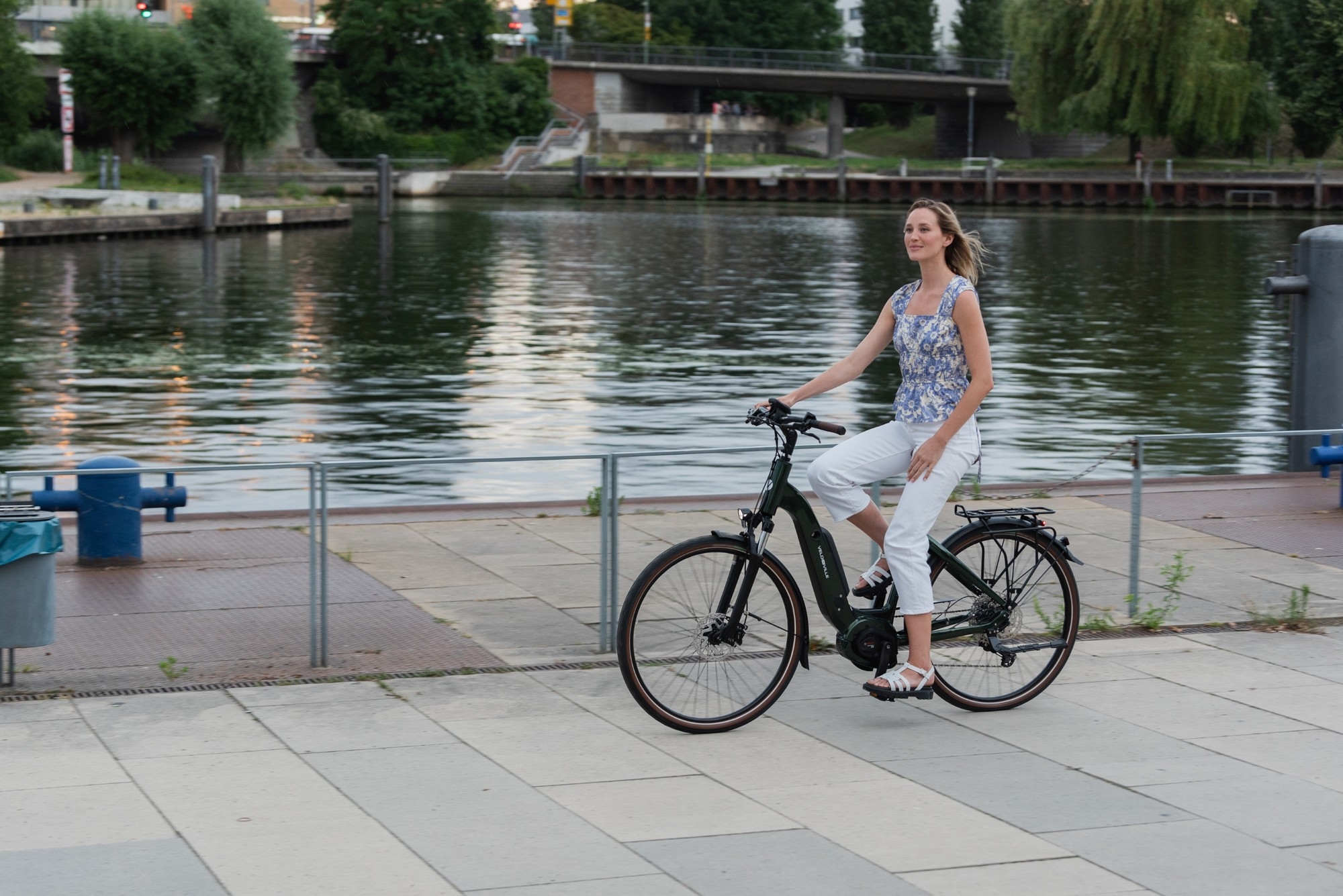 Eine Frau fährt mit ihrem Velo de Ville e-Bike am Wasser entlang, das e-Bike wurde in Ahrensburg geleast.