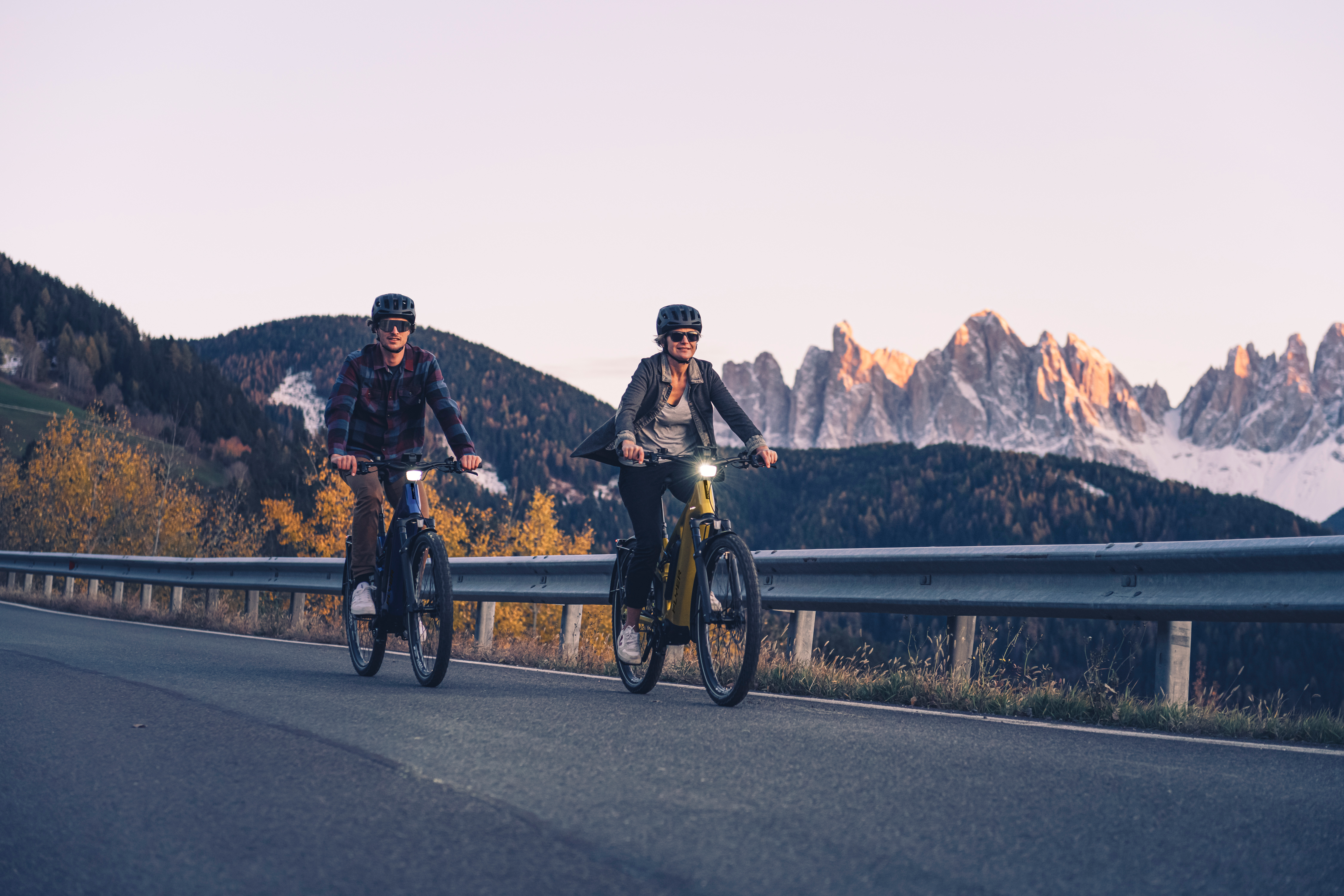 Das Bild zeigt zwei Personen in den Bergen, die auf einer Straße e-Bikes mit einem Pinion MGU Motor fahren.