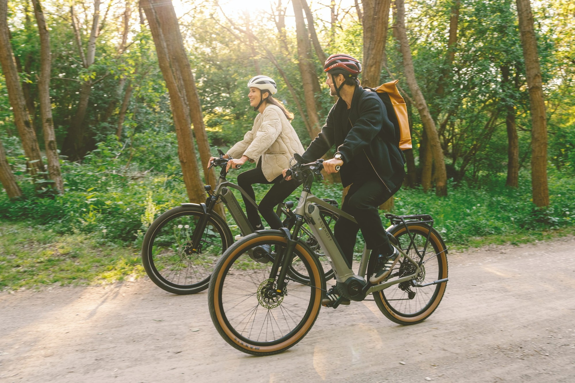Das Bild zeigt zwei Personen, die auf modernen E-Bikes der Marke Kalkhoff durch eine bewaldete Umgebung fahren.